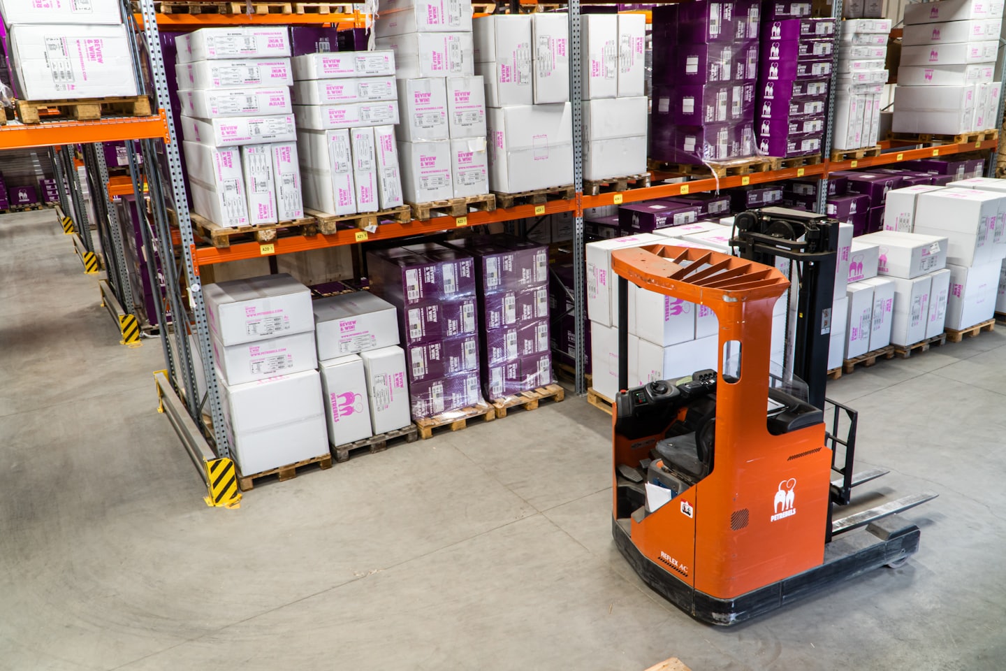 Orange forklift parked in a warehouse aisle with stacked boxes.